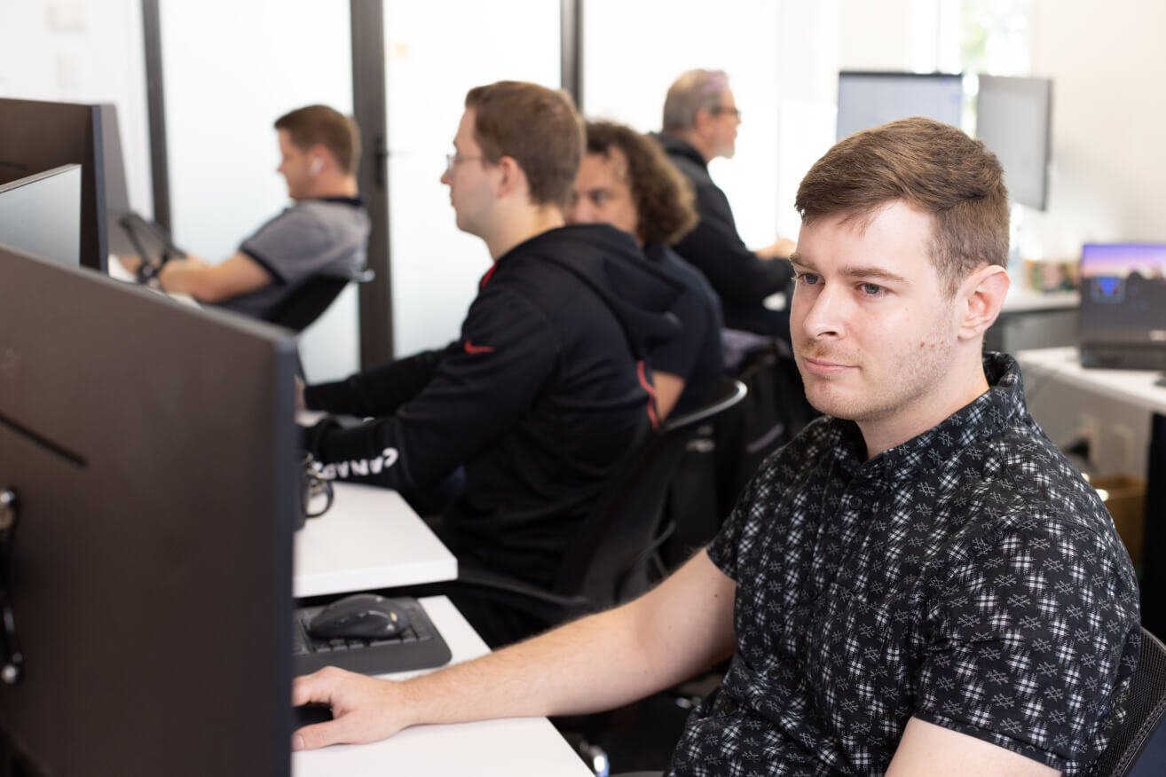 Person sitting in an office with other people working on computers